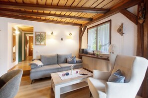 Un salon chaleureux avec un plafond en bois, un canapé, un fauteuil, une table basse et une fenêtre avec des rideaux.