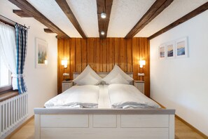 Uma cama com lençóis brancos, painéis de madeira nas paredes e duas luminárias fixadas na parede.
