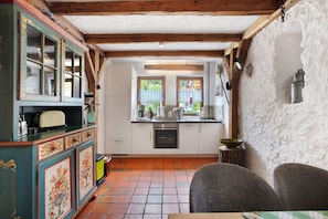 A rustic kitchen with wooden beams, a tiled floor, and a dining area with a table and chairs.