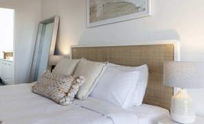 A neatly made bed with white linens and two decorative pillows, a woven headboard, a framed artwork above the bed, and a bedside lamp. - SELLICKS BEACHSIDE RETREAT unwind by the sea (Sellicks Beach)