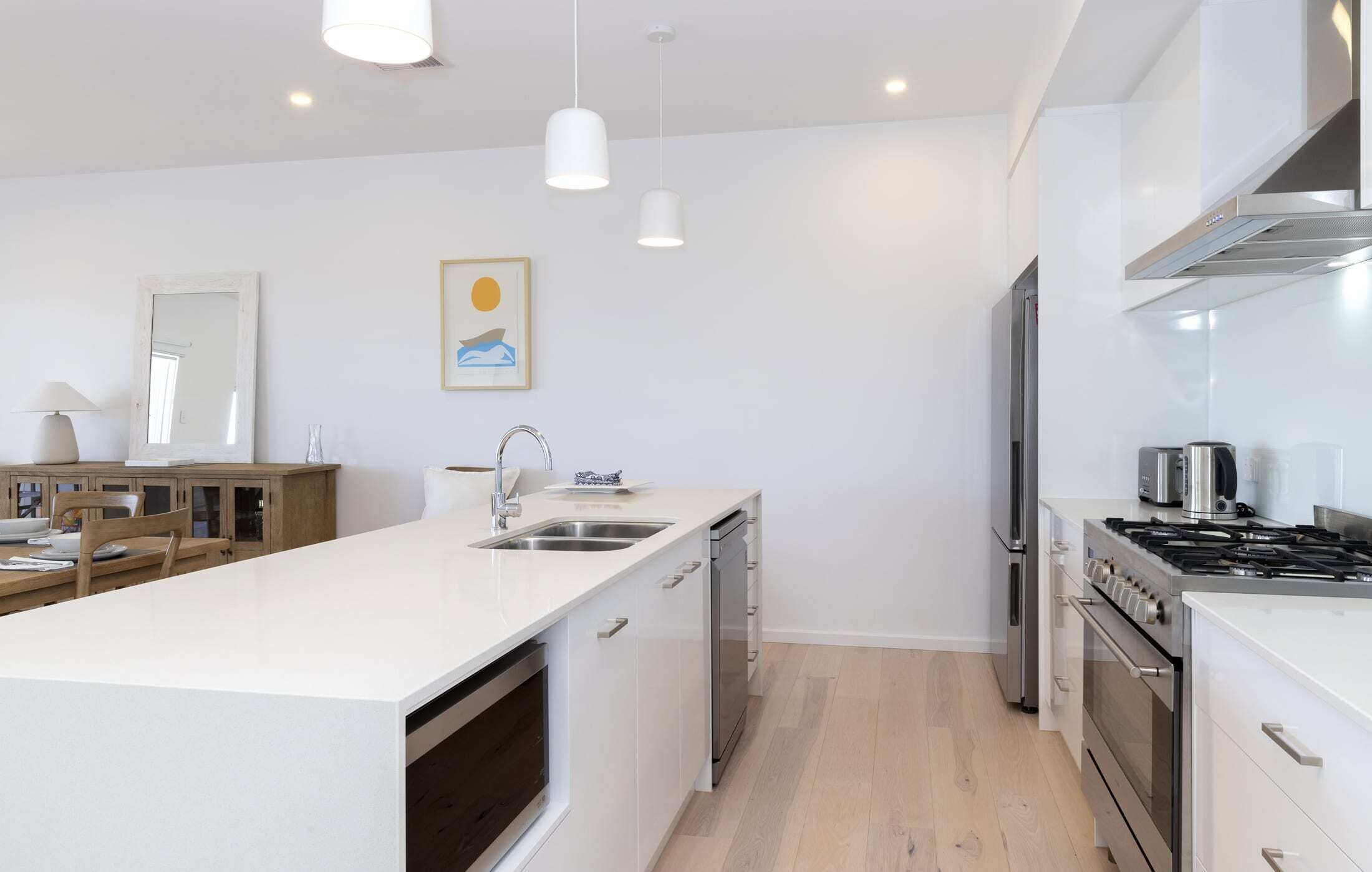 Una cocina moderna con armarios blancos, electrodomésticos de acero inoxidable, una isla central con fregadero e iluminación colgante.