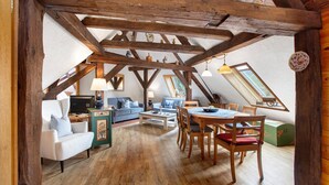 Une pièce de style loft avec des poutres apparentes, une table à manger avec des chaises, un canapé et un petit meuble.