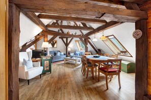 Une pièce de style loft avec des poutres apparentes, une table à manger avec des chaises, un canapé et un petit meuble.