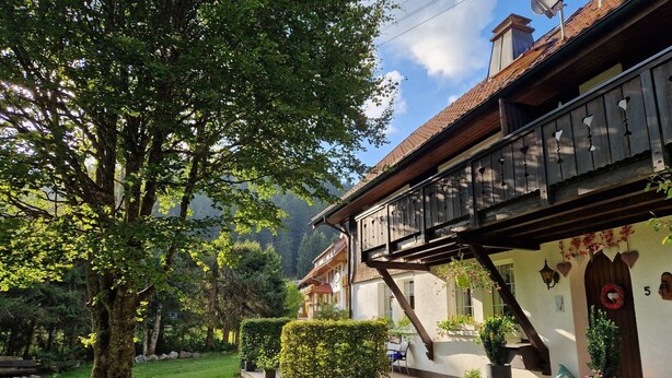 Un chalet traditionnel doté d’un balcon en bois, entouré d’une végétation luxuriante et d’un jardin bien entretenu.