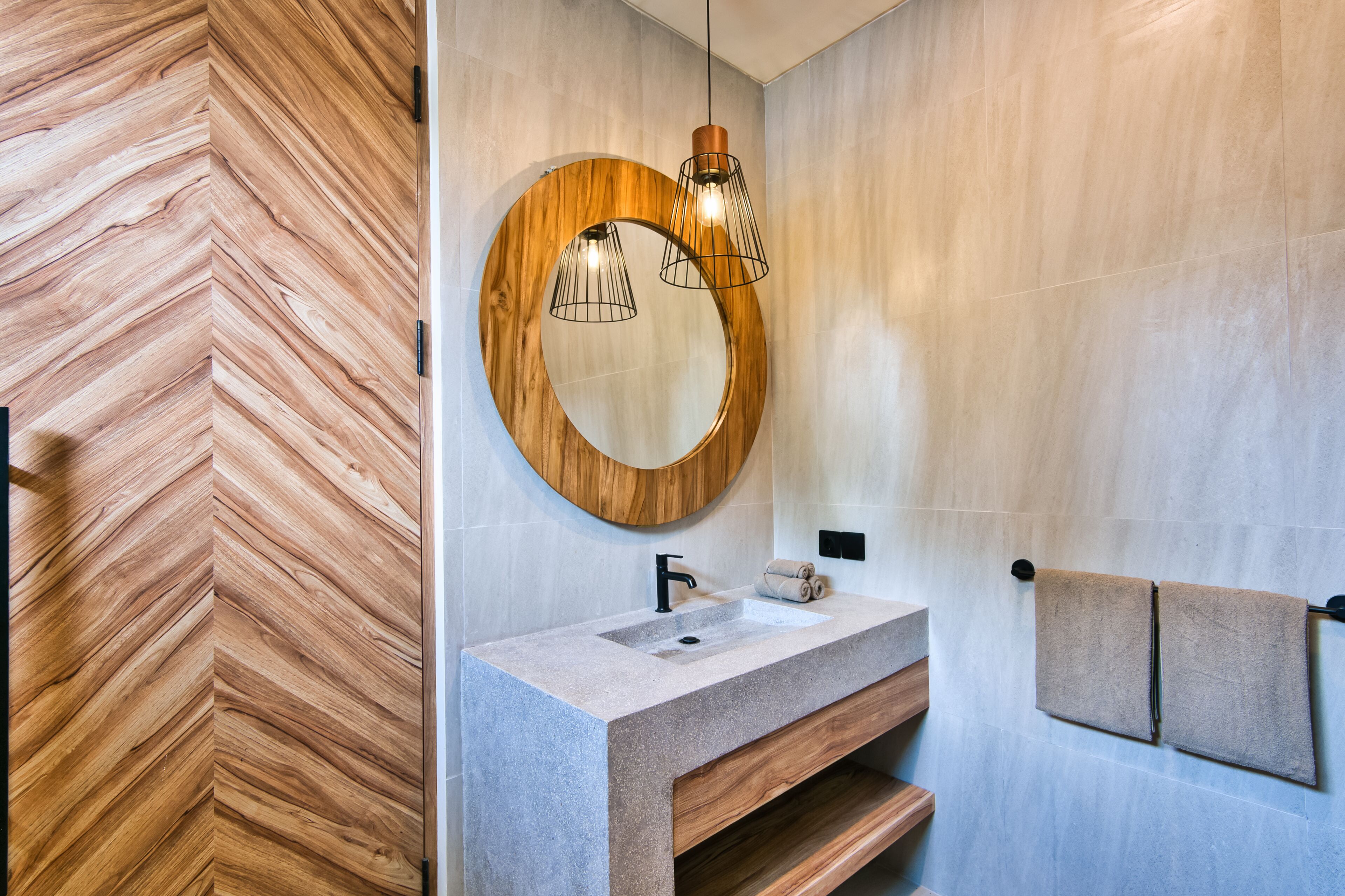 Une salle de bain moderne avec un mur en bois à motifs en chevrons, un miroir rond, un lavabo en granit et un porte-serviettes.