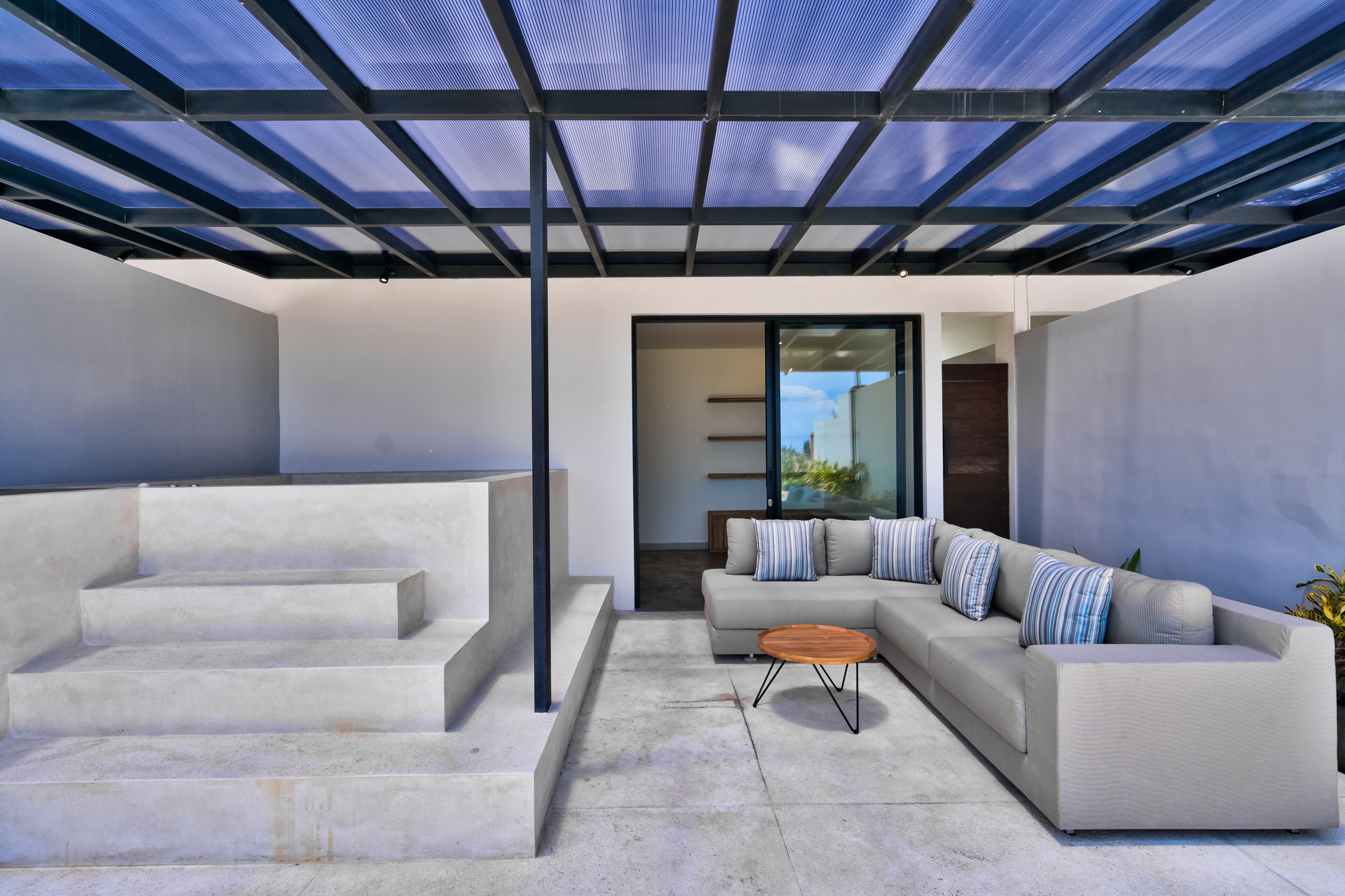 Un'area living esterna moderna con tetto in vetro, un divano e un tavolino in legno.