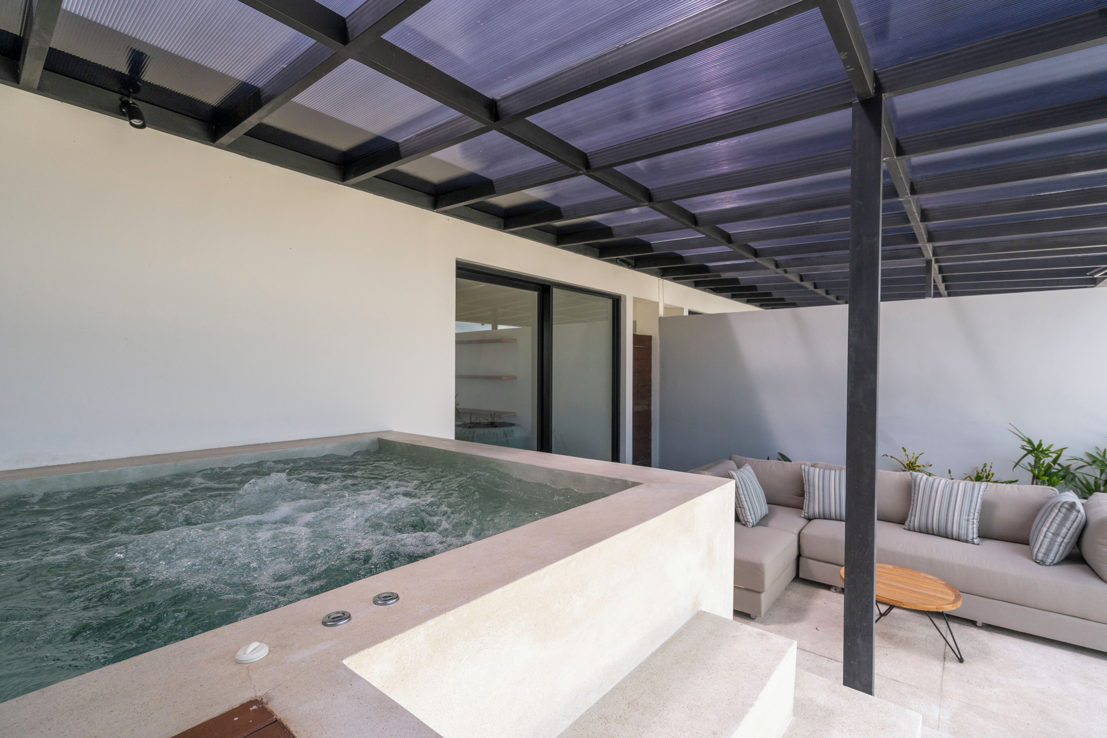 Un espacio exterior moderno con jacuzzi, sofá y una mesita.