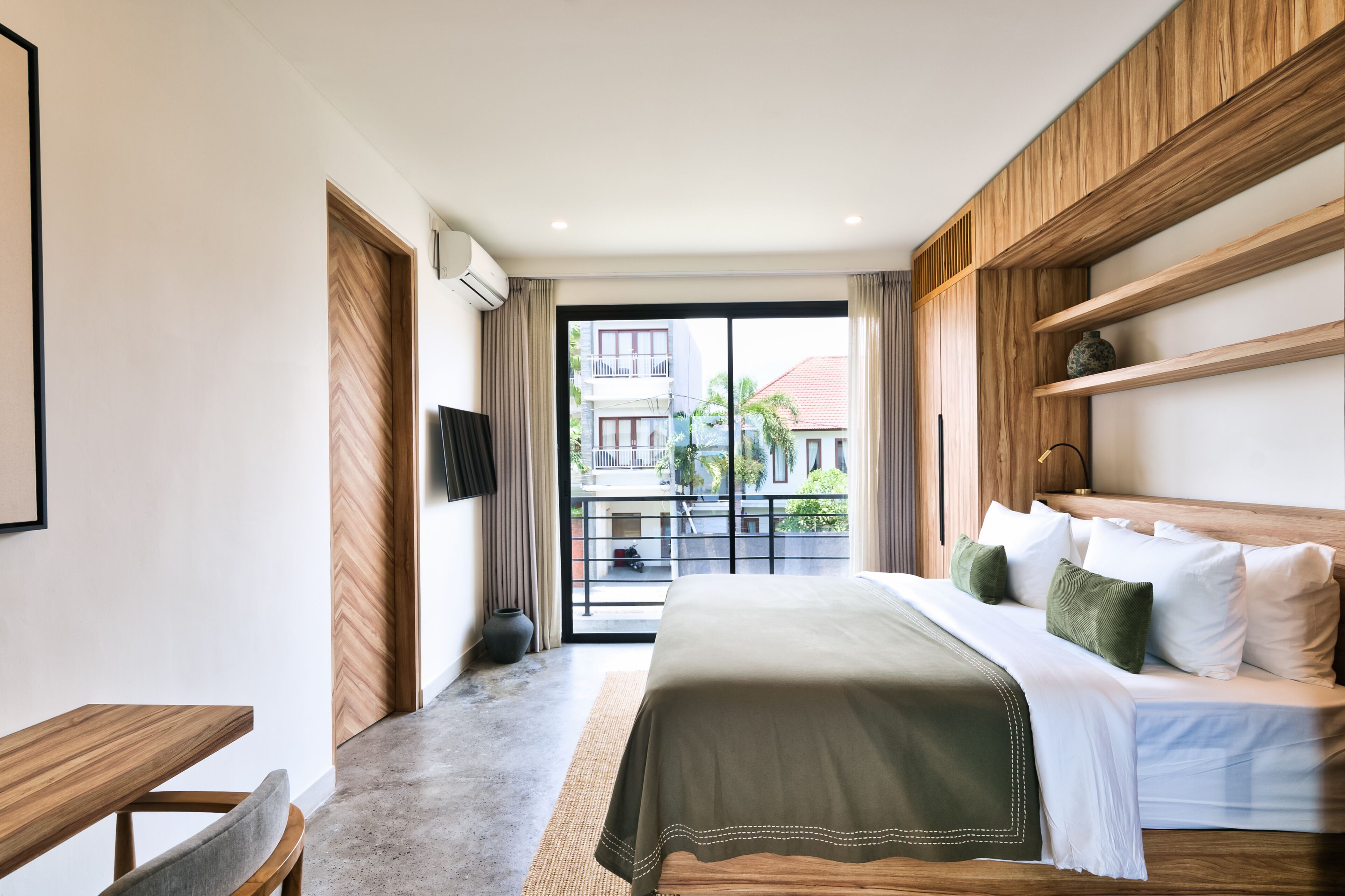 A modern hotel room with a large bed, wooden headboard, and a view of the outside balcony.