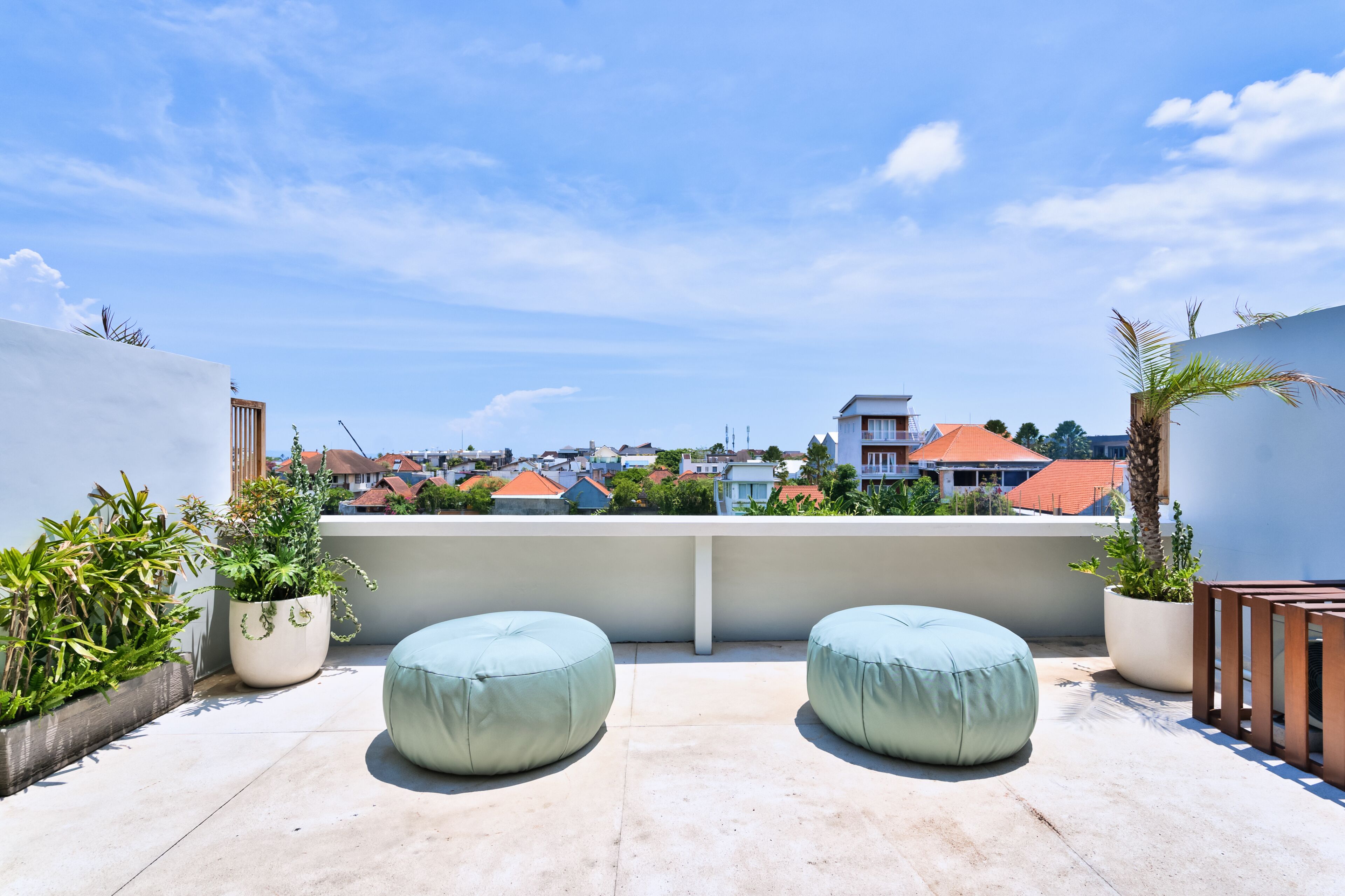 Una terrazza sul tetto con due zone salotto imbottite in celeste, piante in vaso e vista sugli edifici circostanti.