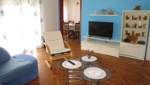 A living room with a sofa, a chair, a TV, a glass coffee table, and a cabinet with decorative items. - Cosy apartment for 6 guests with A/C, WIFI, TV, terrace and pets allowed (Zadar)