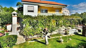A two-story house with a tiled roof, a small garden with grapevines, and a stone staircase leading to the entrance. - Cosy apartment for 6 guests with A/C, WIFI, TV, terrace and pets allowed (Zadar)