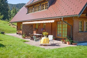 Ein Haus mit rotem Ziegeldach, einer überdachten Terrasse mit Gartenmöbeln und einer Ziegel-Fassade.