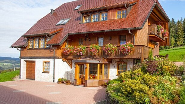 Et traditionelt chalet-hus med skråtag, træbalkoner med blomsterkasser og en stenfasad.