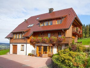Ein traditionelles Chalet mit einem geneigten Dach, Holzbalkonen mit Blumenkästen und einer Steinfassade.