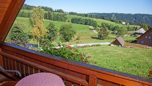 Een balkon met uitzicht op een landelijk landschap, met groene velden, bomen en huizen.