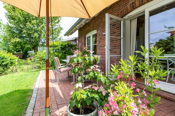 Ein Terrassenbereich mit Backsteinboden, Blumentöpfen und einem Tisch mit Stühlen.
