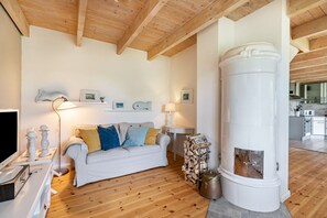 A living room with a white sofa, wooden flooring, a fireplace, and a kitchen in the background.