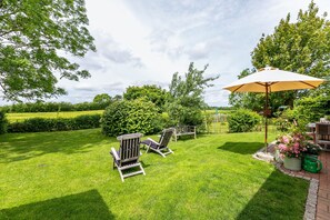 A well-maintained lawn with two Adirondack chairs, a wooden bench, and a patio umbrella.