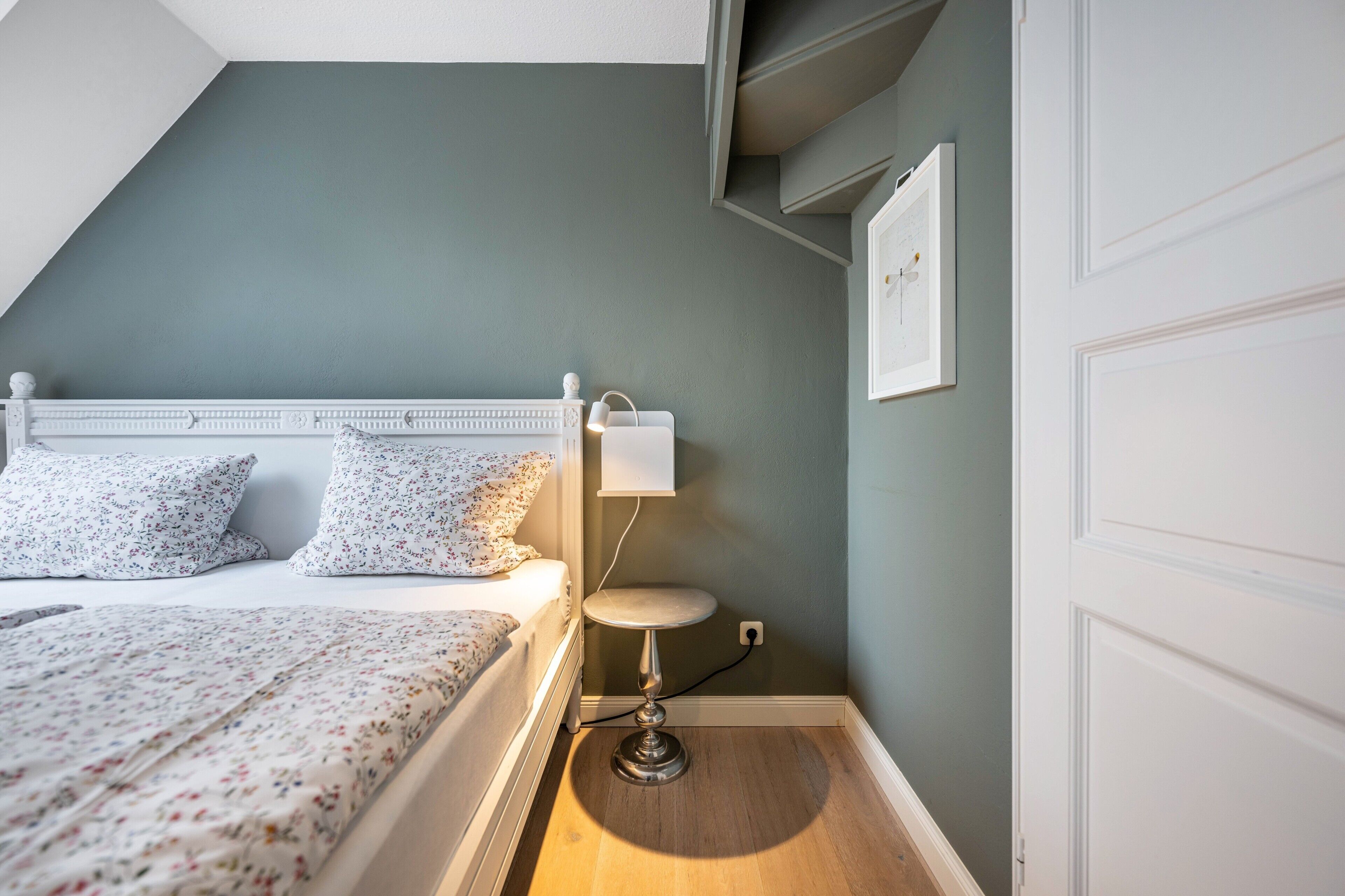 Une chambre à coucher avec un lit, une table de chevet, une lampe et un tableau accroché au mur.
