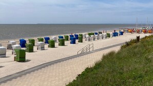 En strand med rækker af strandstole og parasoller, en belagt sti og udsigt til havet.