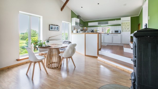 A modern kitchen with wooden flooring, a dining area with white chairs, and a view of the outdoors through large windows. - Holiday Apartment "Alter Heuboden" with Private Garden, Panoramic Views and Wi-Fi (Steinbergkirche)