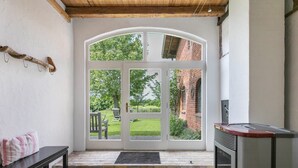 A room with a stone floor, a bench, a fireplace, and a large arched window with a view of a garden. - Holiday Apartment "Alter Heuboden" with Private Garden, Panoramic Views and Wi-Fi (Steinbergkirche)
