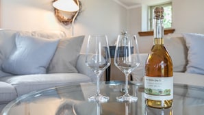 A bottle of wine on a glass table with two empty wine glasses, a sofa, and a wall-mounted lamp in a living room. - Holiday Apartment "Alter Heuboden" with Private Garden, Panoramic Views and Wi-Fi (Steinbergkirche)
