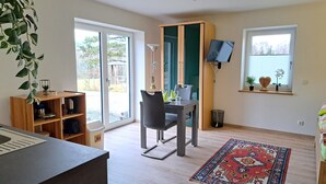 Una cocina moderna con horno empotrado, un comedor con mesa y sillas, un ventanal grande y un televisor montado en la pared.