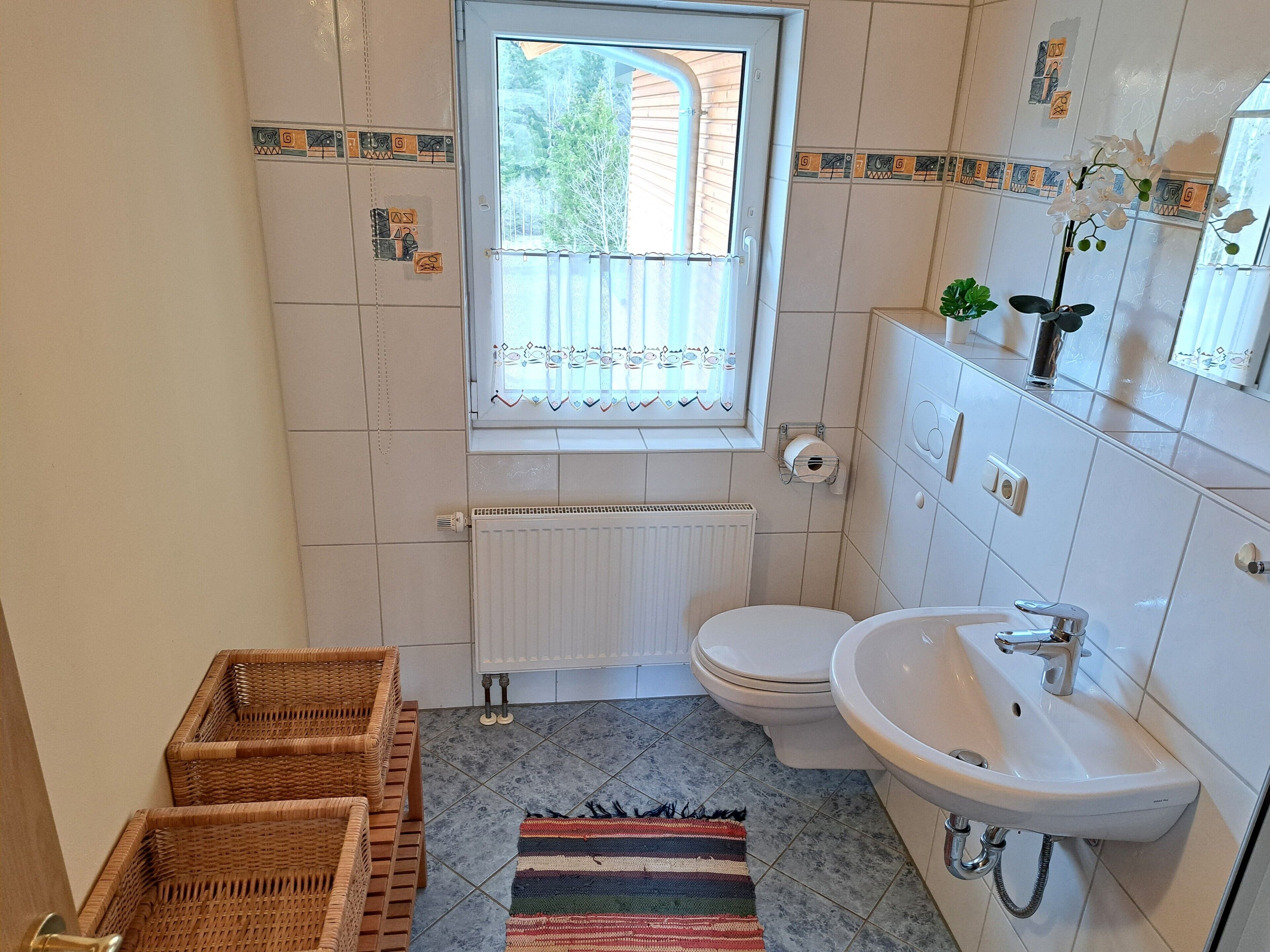 A bathroom with a toilet, sink, window, radiator, and wicker baskets.