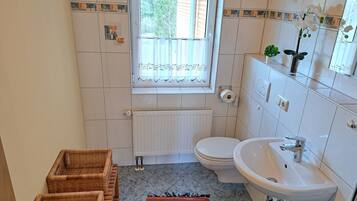 A bathroom with a toilet, sink, window, radiator, and wicker baskets.
