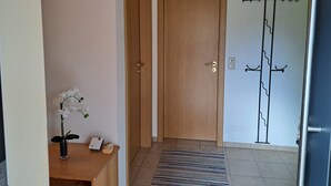 A hallway with a wooden door, a coat rack, a small table with a flower vase, and a rug.