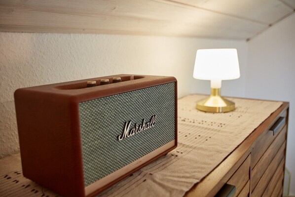 Un altavoz Marshall antiguo sobre una cómoda de madera con una lámpara al fondo.