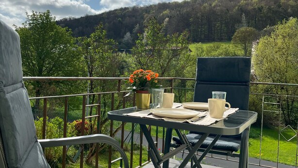 Una terraza con mesa y sillas, con vista a un paisaje boscoso.