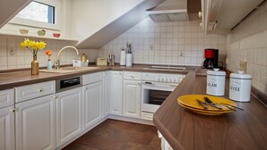Una cocina con armarios blancos, encimera de madera, cafetera y un plato amarillo con cubiertos.