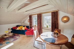 A room with a blue sofa, red chairs, a round dining table, and a window with curtains. - Apartment 'Angernest' with Shared Garden, Balcony and Wi-Fi (Elfershausen)