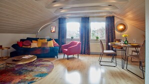 Un acogedor loft con un sofá azul, una silla rosa, una mesa de comedor con sillas y una alfombra colorida.