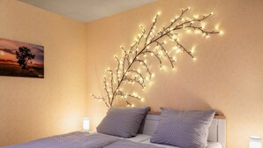 Un dormitorio con cama, almohadas, mesita de noche, lámpara de pared y un cuadro.