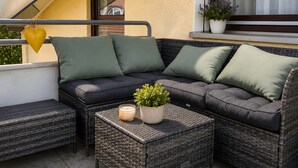 An outdoor seating area with a sofa and two side tables, a potted plant, and a heart-shaped decoration. - Retreat Apartment with Mountain View, Balcony, and Wi-Fi (Langenargen)