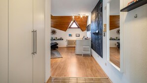 A narrow hallway with a sloped ceiling, wooden beams, a radiator, a small stool, and a radiator. - Retreat Apartment with Mountain View, Balcony, and Wi-Fi (Langenargen)