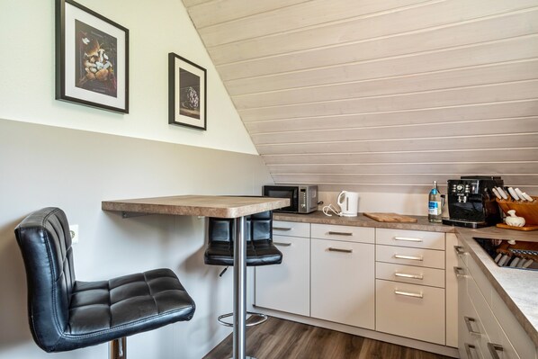 A kitchen with a bar stool, a microwave, a kettle, and a coffee maker.
