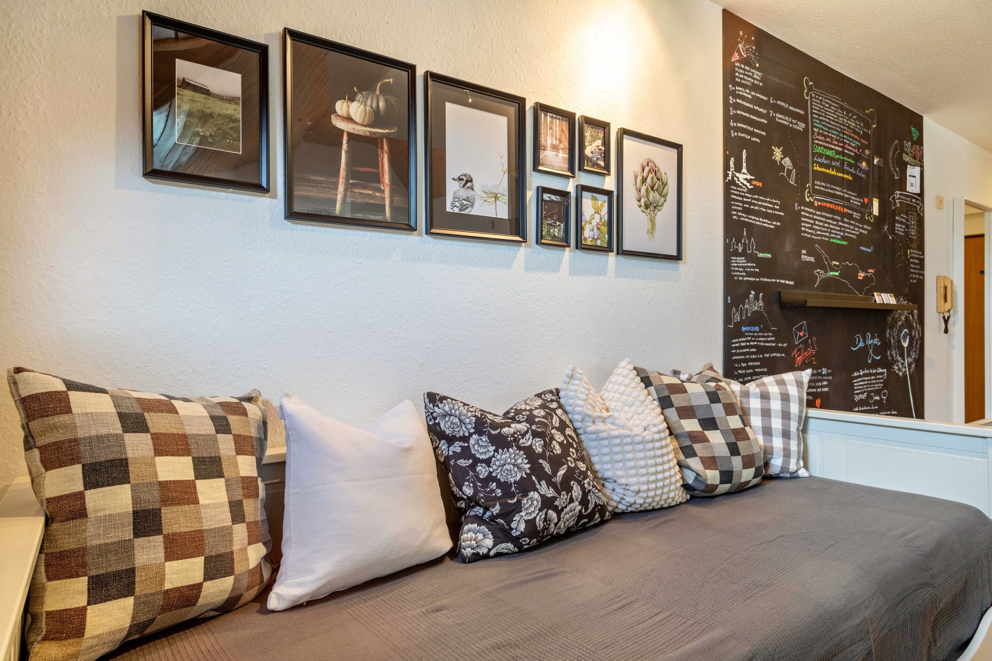 A room with a bed, a wall with framed pictures, and a chalkboard with writing.