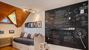 A bedroom with a sloped ceiling, a bed, a small stool, and a wall with chalkboard writing. - Retreat Apartment with Mountain View, Balcony, and Wi-Fi (Langenargen)