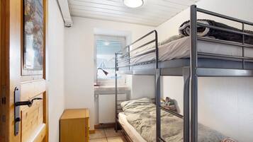 Ein Schlafsaalzimmer mit Etagenbetten, einem Schreibtisch, einem Fenster und einer Heizung.