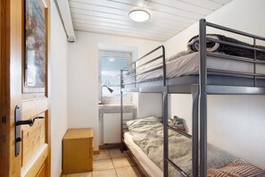 Une chambre de dortoir avec des lits superposés, un bureau, une fenêtre et un radiateur.