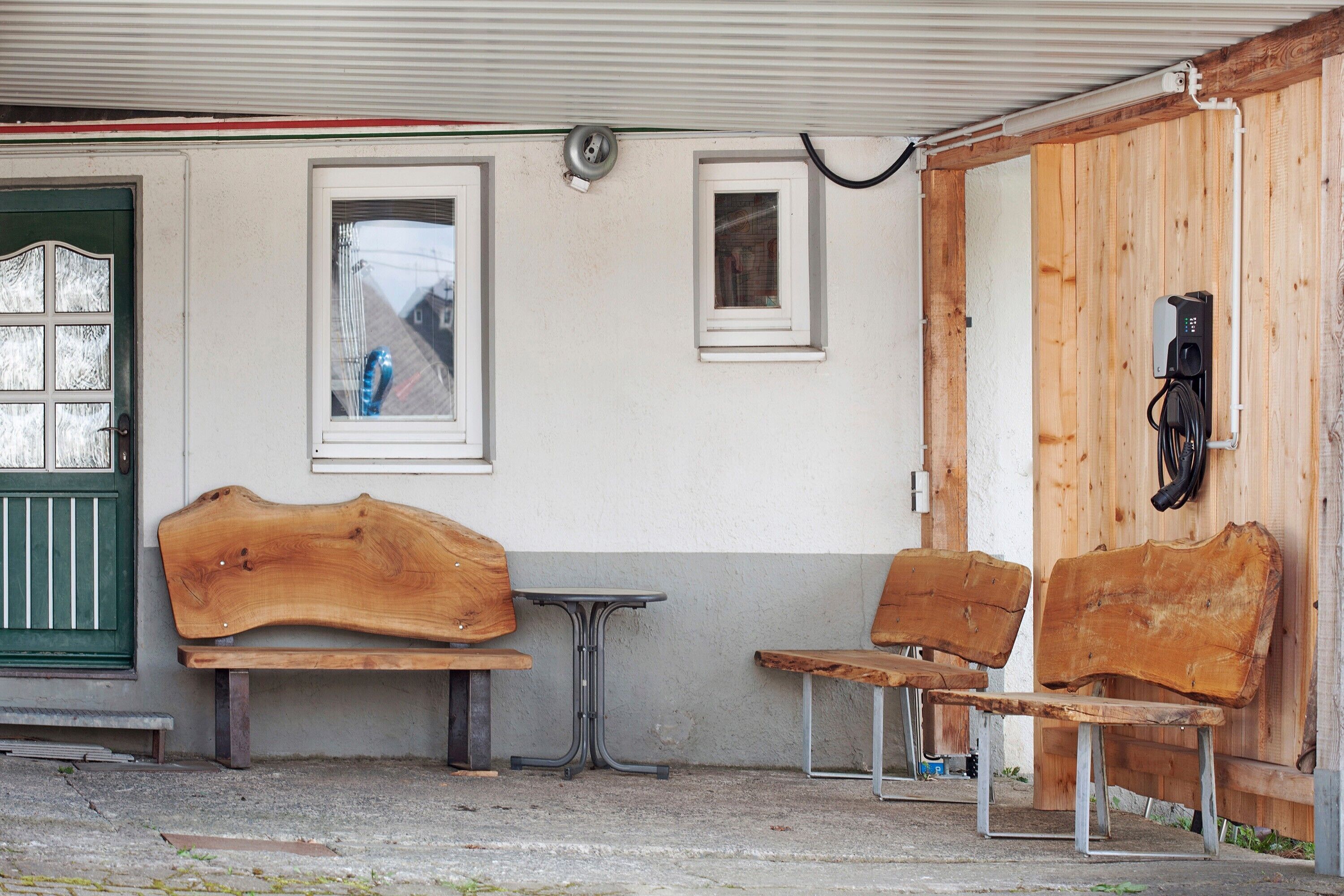 Ein Gebäude mit einer grünen Tür, zwei hölzernen Bänken, einem kleinen Tisch und einer Holzwand mit Steckdose.