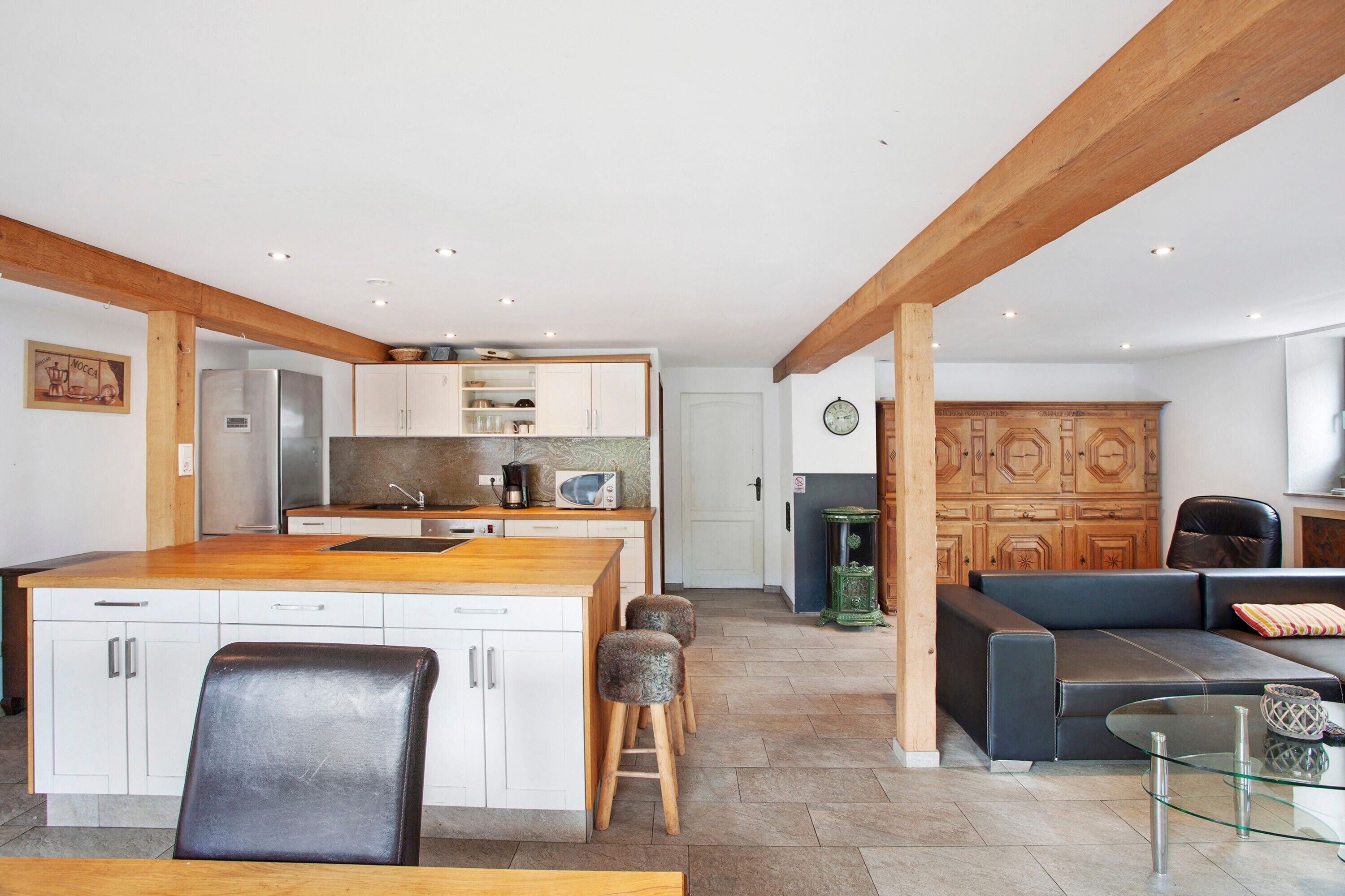 Una cucina moderna con isola centrale, zona pranzo con tavolo in vetro e angolo living con divano e tavolino.