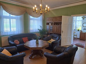 A living room with a black leather sofa, a wooden coffee table, and a chandelier. - Holiday Home 'Hof Schumacher' with Shared Terrace, Garden, and Wi-Fi (Gumtow)