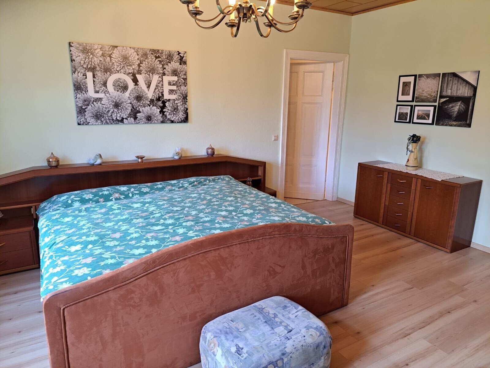A bedroom with a bed, a chest of drawers, a door, and a wall with a 'LOVE' sign.