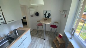 A kitchen with a sink, stove, and cabinets, a small dining table with two chairs, and a window with a view of the outdoors.