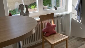 Keittiössä on puinen pöytä, punaisella tyynyllä varustettu tuoli ja ikkuna, josta avautuu näkymä puutarhaan.
